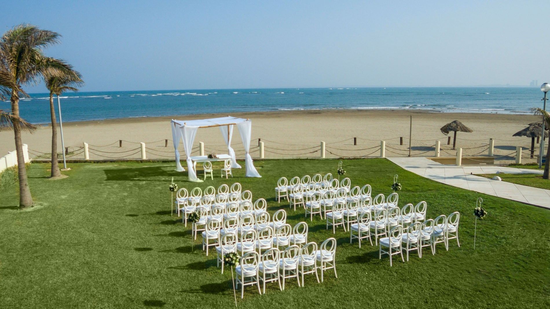 Beautiful outdoor wedding ceremony set on a green lawn overlooking the ocean beach at Camino Real Veracruz