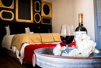 Wine glass and bottle on a tray by a bed under gold frames in a room at NOI Blend Colchagua, Chile