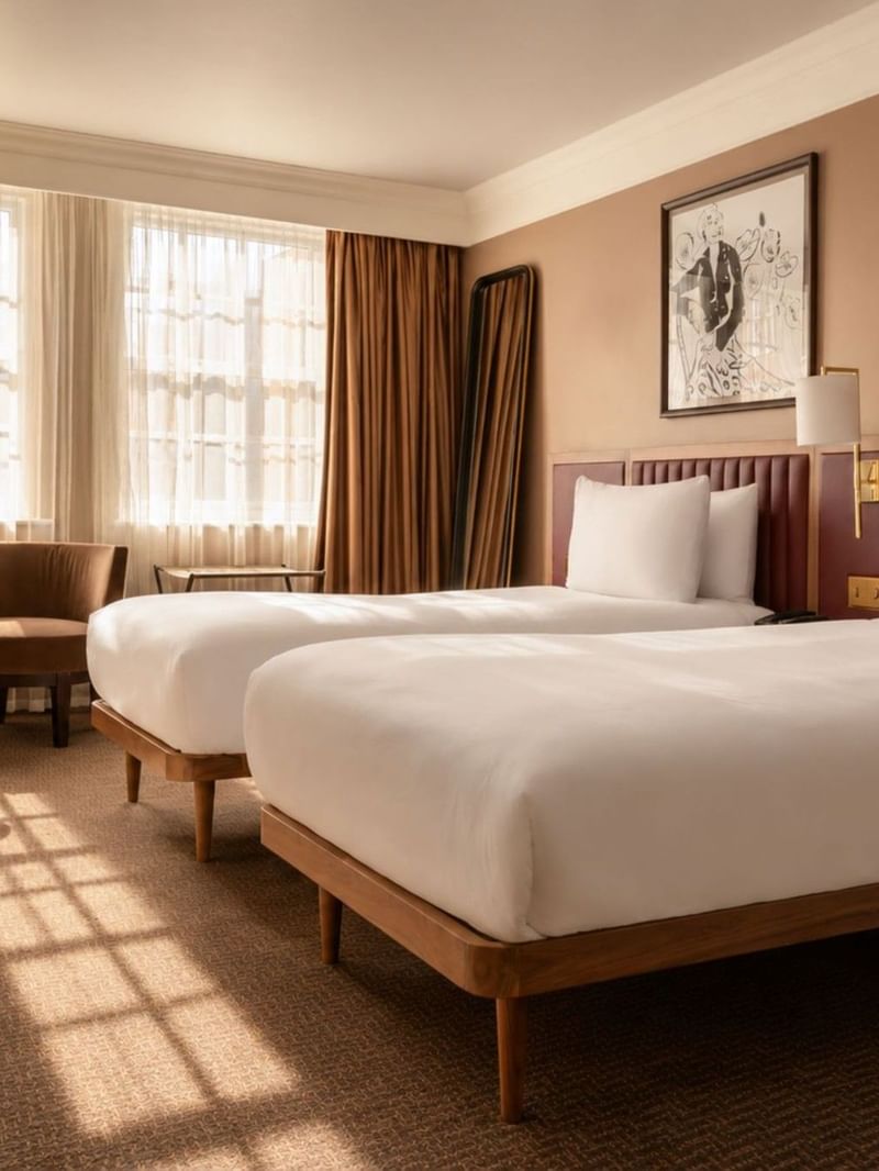 Bright Collection Deluxe Twin room with two beds, brown upholstered headboards, seating area, and large windows with drapes at The May Fair Hotel, London