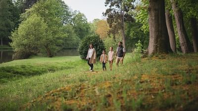 Une famille se promène dans un parc verdoyant bordé d'arbres et d'un étang en automne pour l'Offre Été Indien