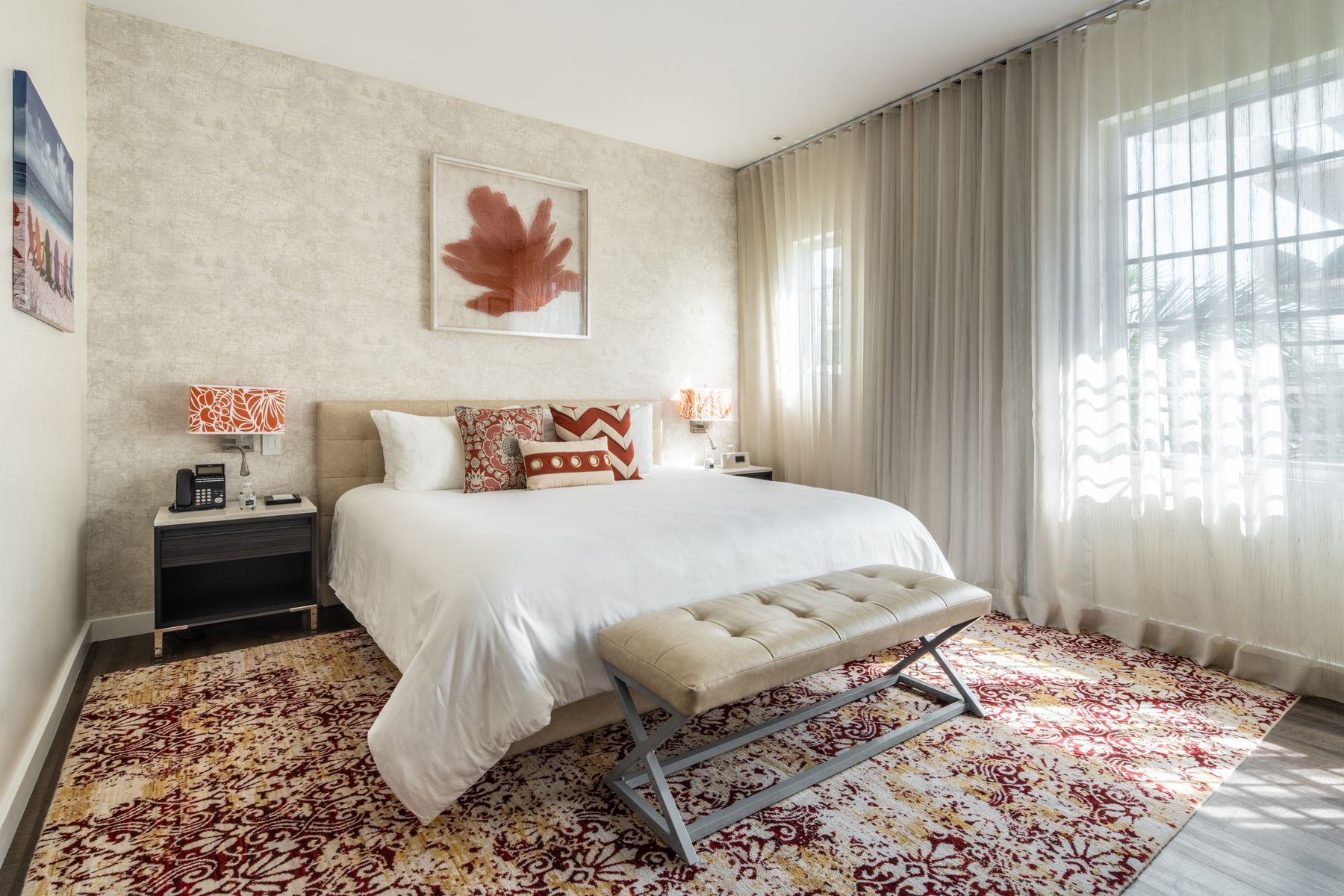 A wide view of a hotel room with a large bed, nightstands, and a window with sheer curtains.