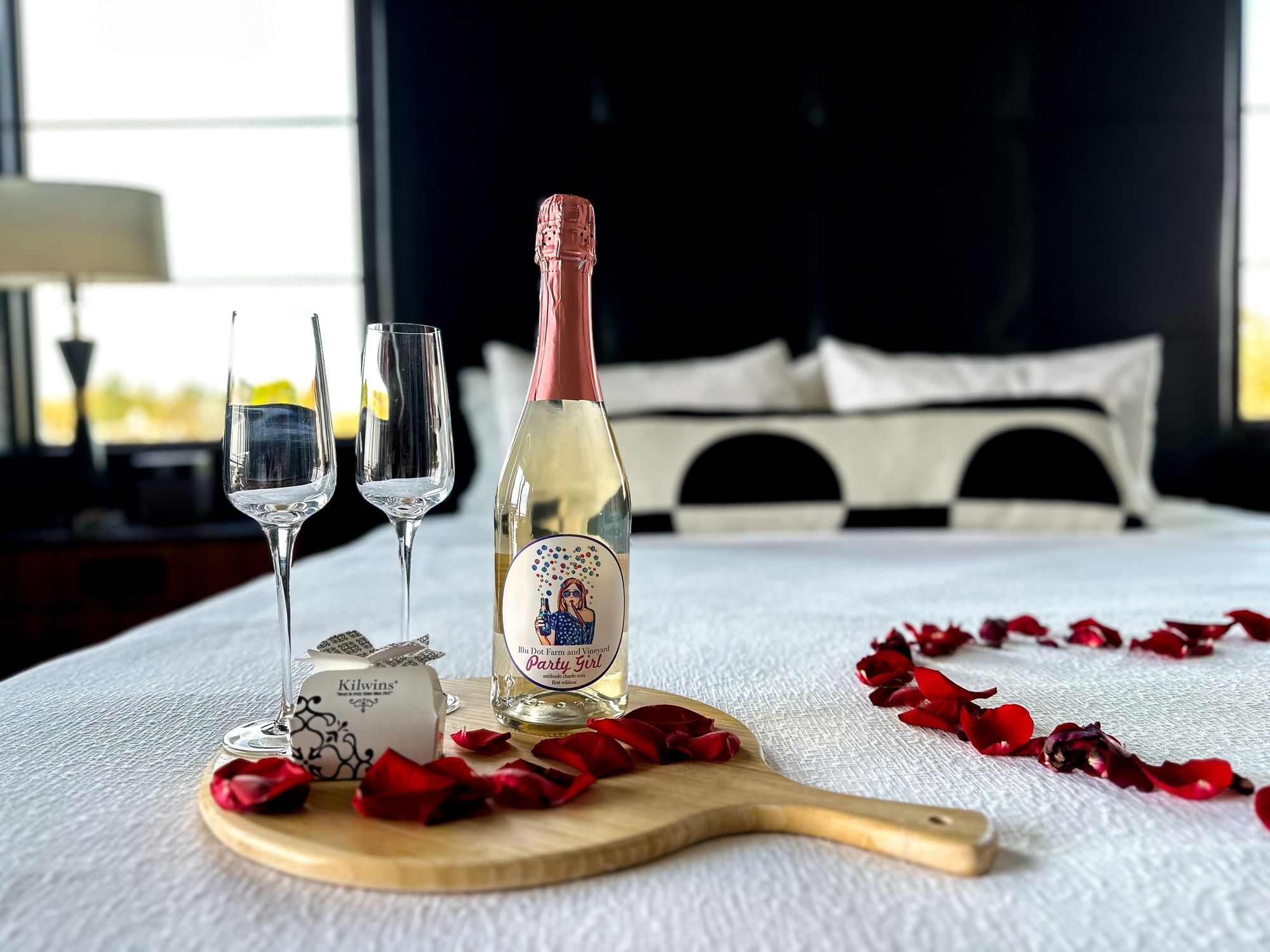 Party Girl sparkling wine bottle and champagne glasses arranged on a bed with rose petals at The Earl