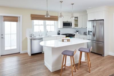 Winnapaug Pond kitchen featuring white cabinetry, stainless steel appliances, and two bar stools at The Hotel Maria