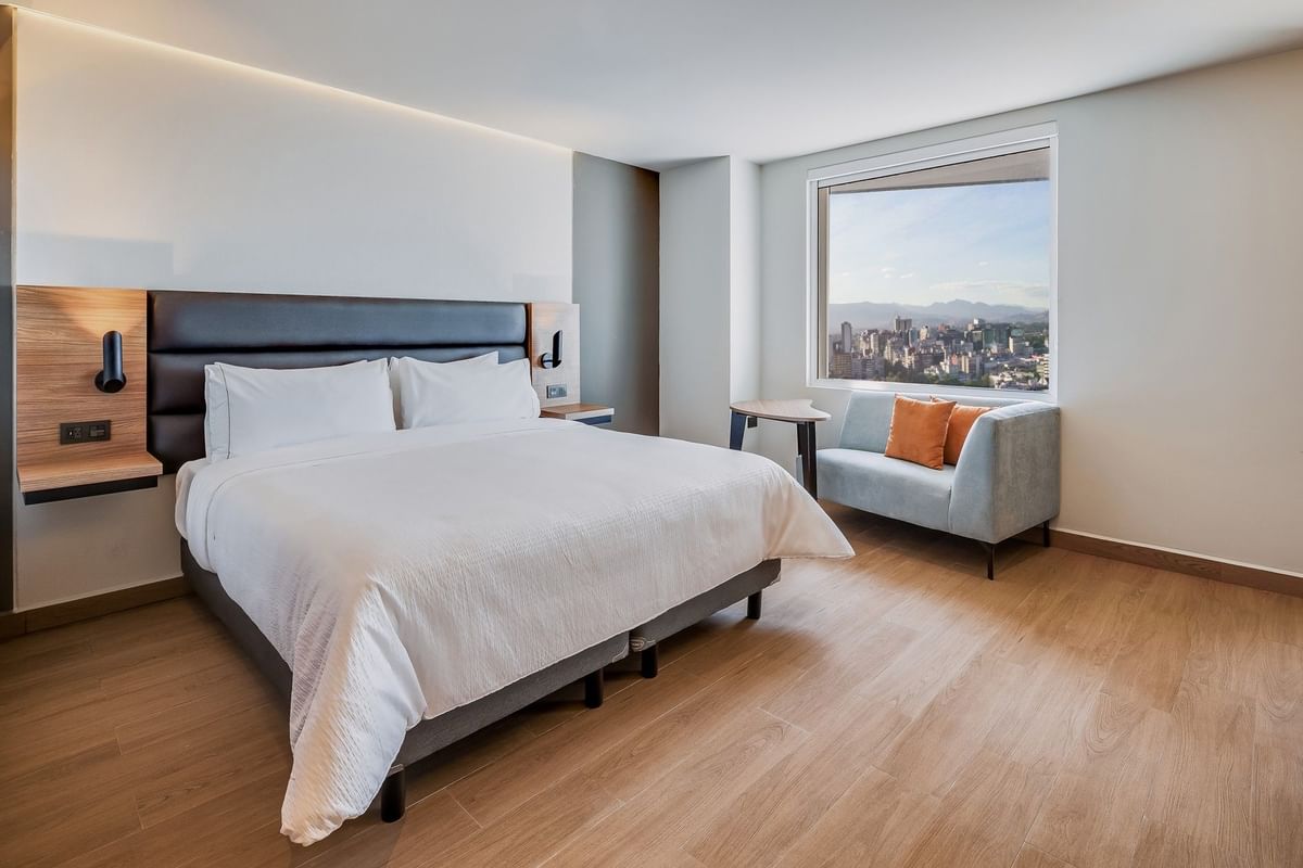 Habitación luminosa con cama king y área de estar con vista a la ciudad en Fiesta Inn
