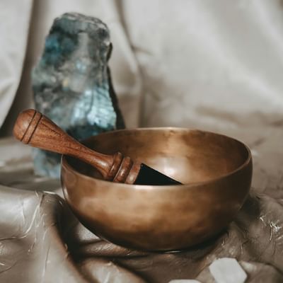 Bronze Klangschale mit Holzschlägel und blauem Kristall auf Stoffhintergrund.