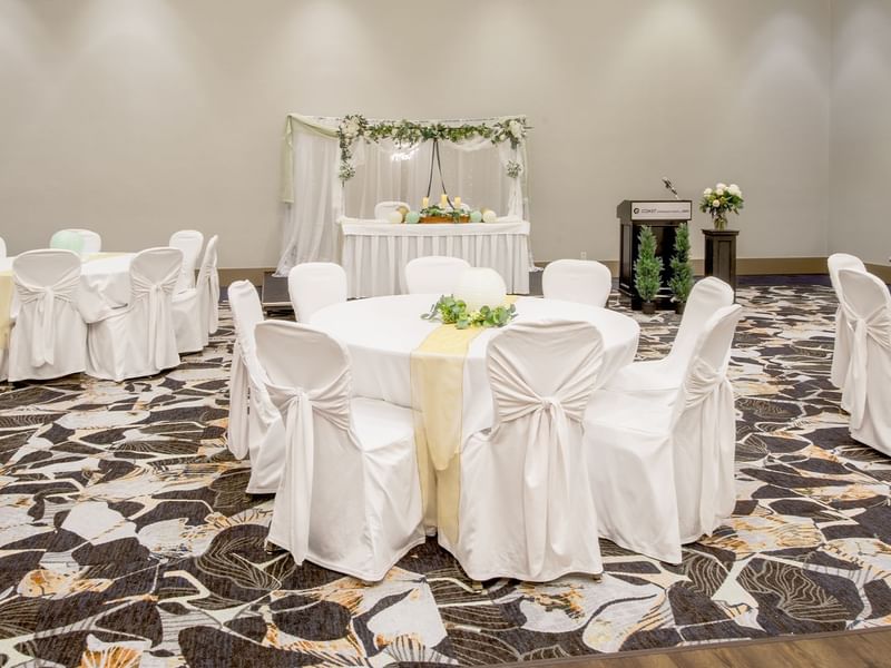 Banquet hall with round tables, draped chairs, and a decorated stage for a wedding.
