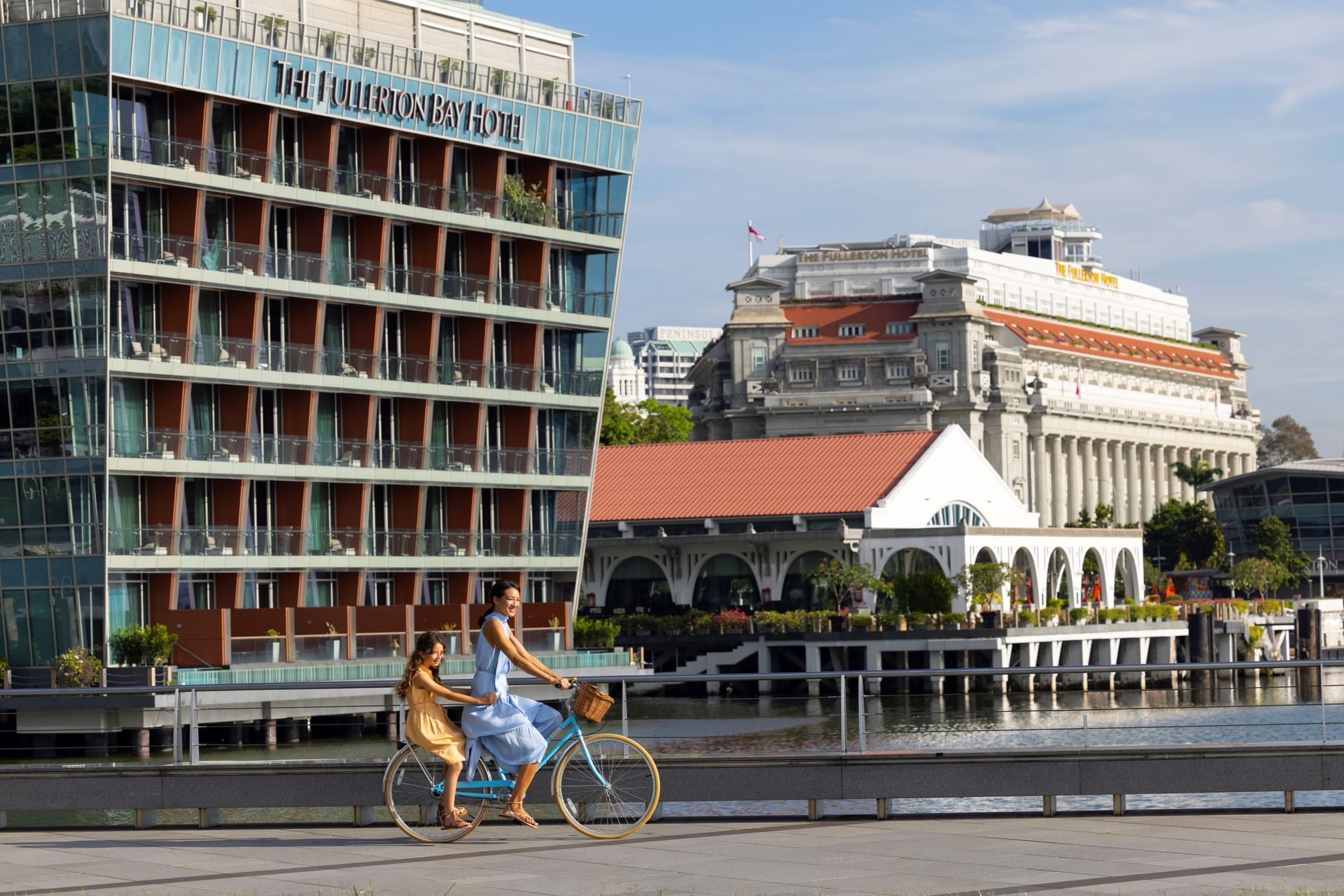 Mother & daughter cycling on the road near The Fullerton Hotels and Resorts