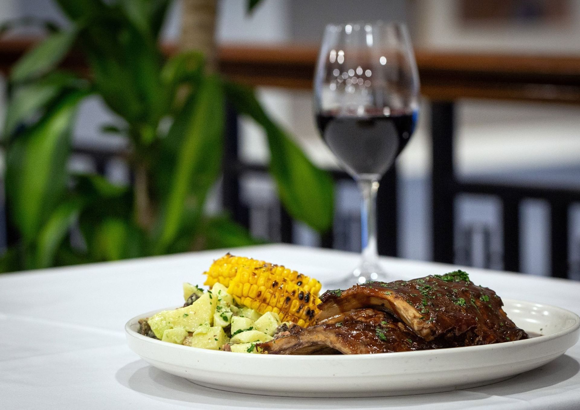 Plate of grilled ribs, corn, and potatoes with a wine glass at Hotel Grand Chancellor Adelaide