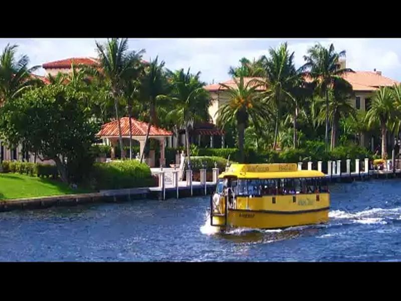 yellow water taxi with homes and palm trees in background
