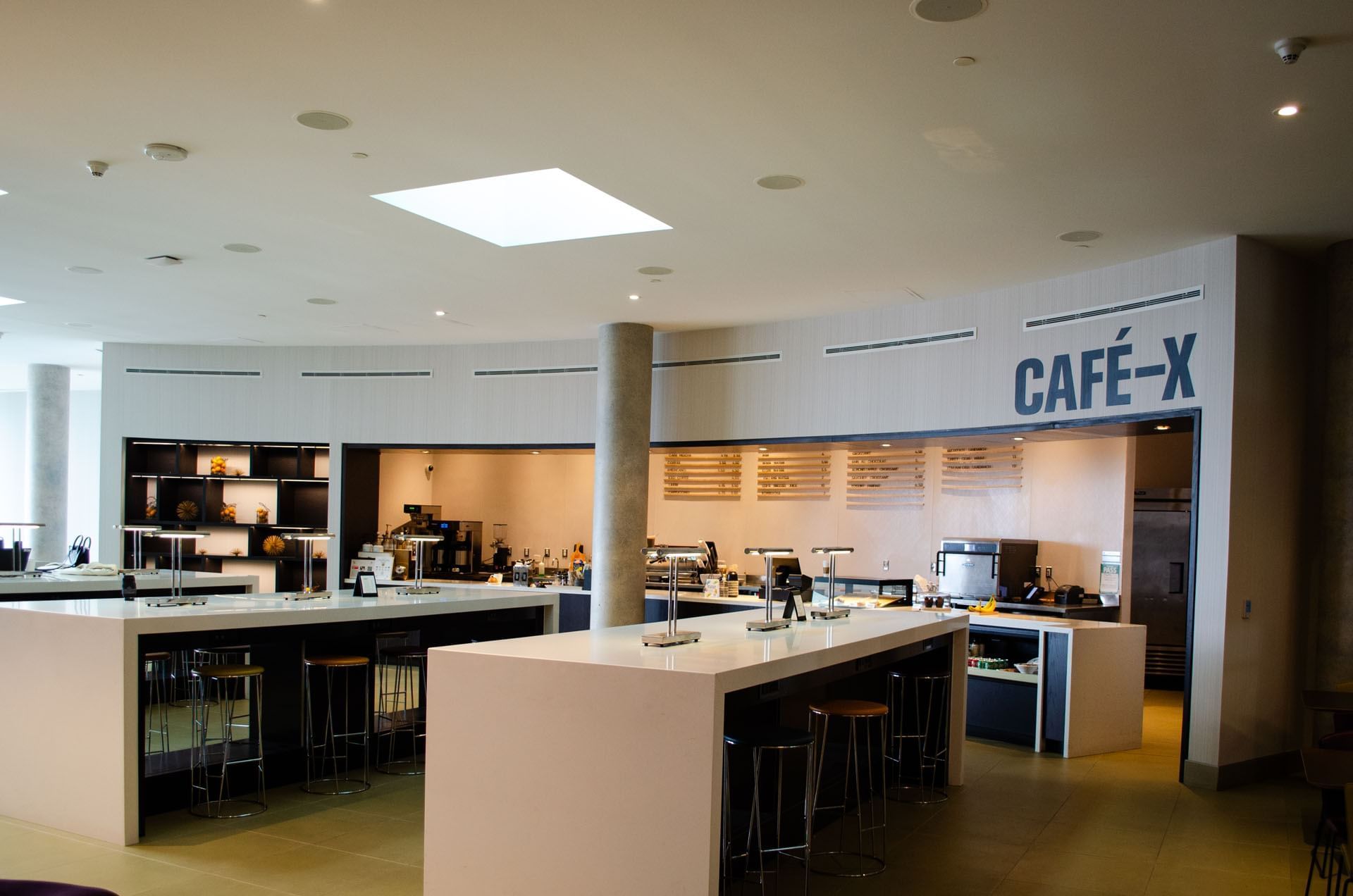 Modern Café-X counter with white high-top seating and menu boards inside dining area at Hotel X Toronto