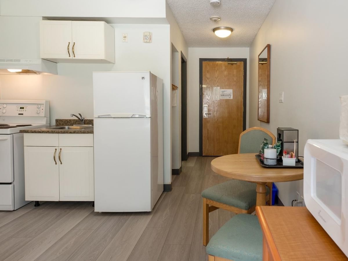 A kitchen with white appliances, a dining table with chairs, and a microwave on a wooden table.