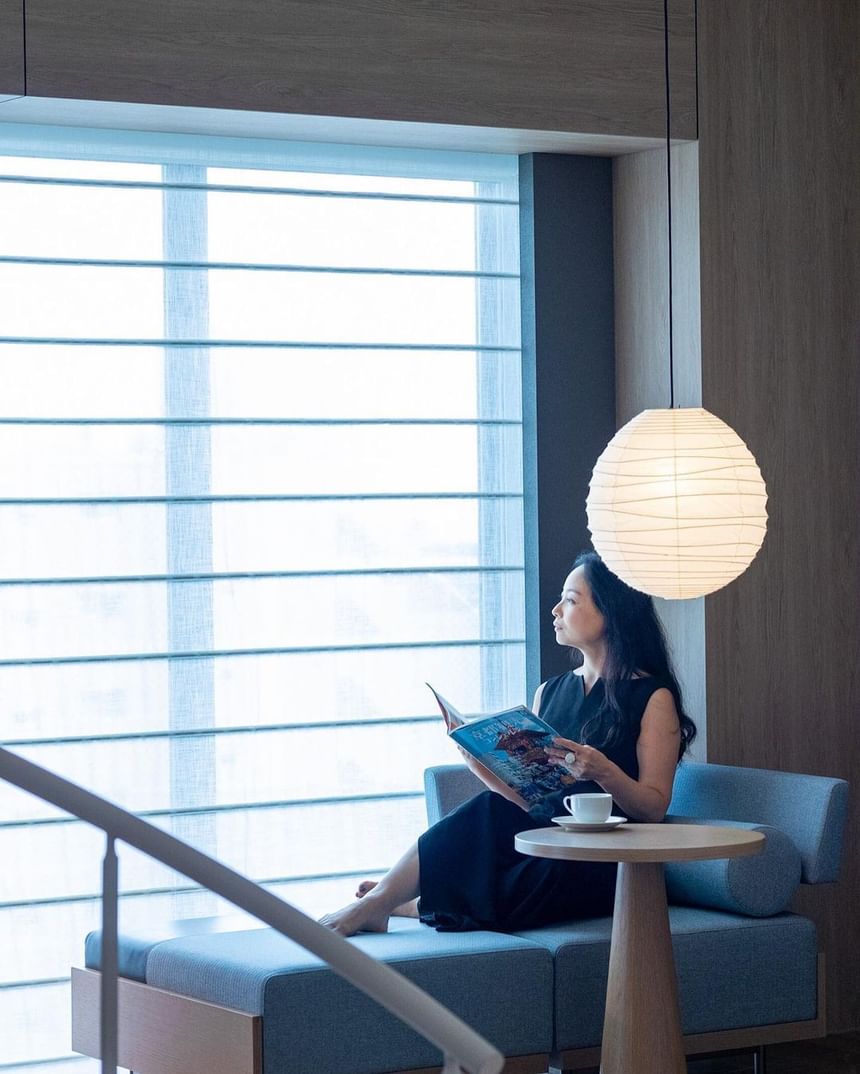 Woman holding a magazine by a window with a hanging lamp at Park Hotel Group