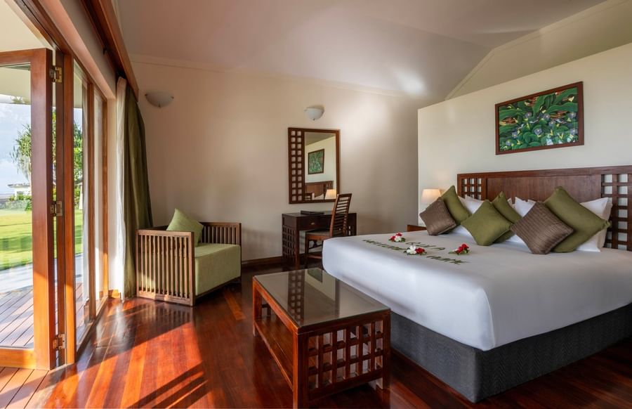 Spacious hotel room with wooden floors, large bed, and balcony at The Naviti Resort - Fiji.