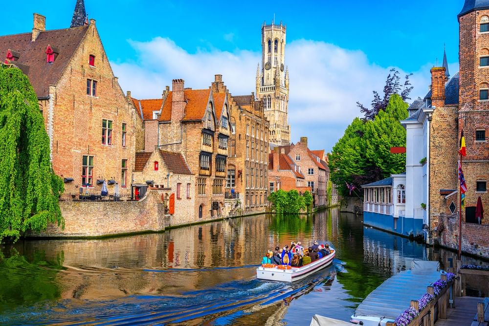 Tourist boat filled with passengers by a canal, surrounded by historic brick buildings near Warwick Grand Place Brussels