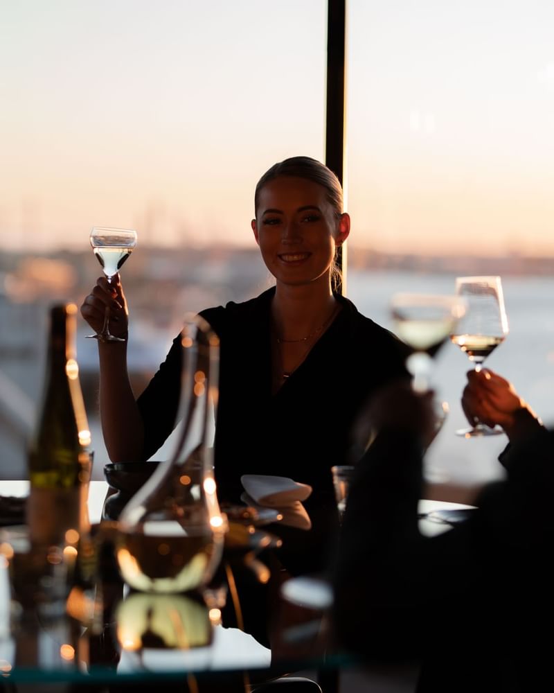 Kvinna i elegant svart klänning håller ett glas vitt vin vid en bordsduk.