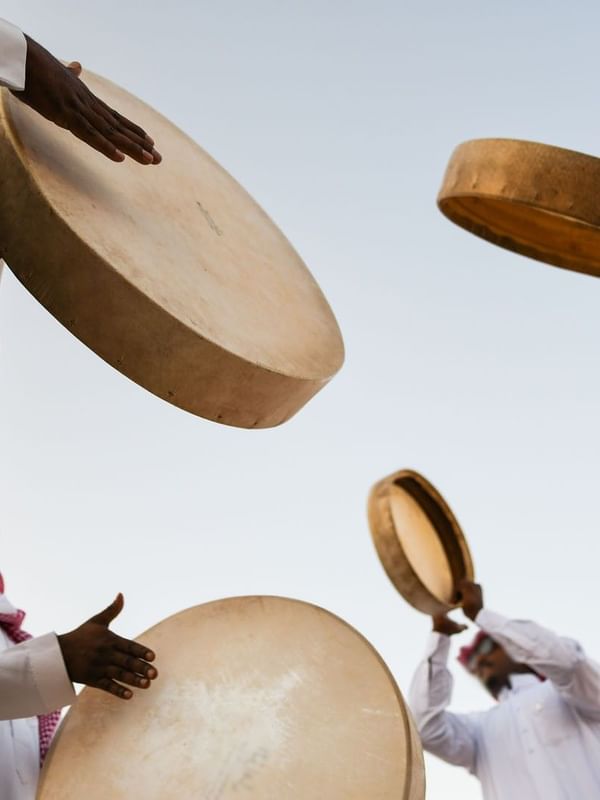 People in traditional Saudi clothing playing large hand drums outdoors at Saja Warwick Madinah