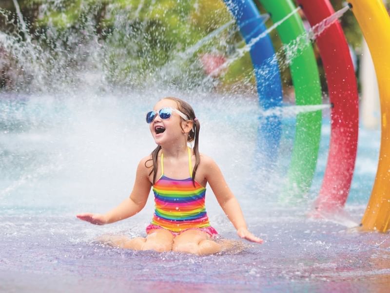 Niña riendo en el parque acuático colorido de Fiesta Americana Funeeq bajo chorros y fuentes vibrantes
