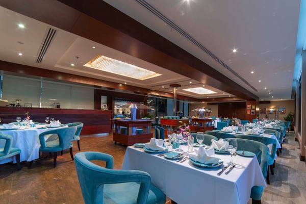 Italian restaurant interior with teal armchairs by tables with white cloths and orchids at Warwick Al Khobar