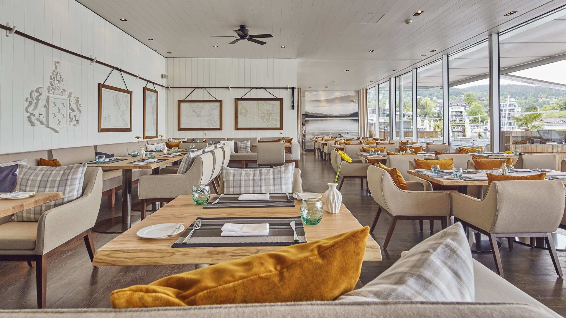 Sala ristorante con tavoli, sedie, centrotavola, mappe sulle pareti e vista sul paesaggio esterno.