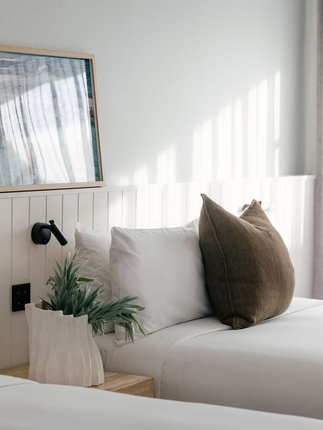 Sunset View Two Bedroom at Elysium Hotels twin beds beside framed coastal art, a plant, and soft grey curtains
