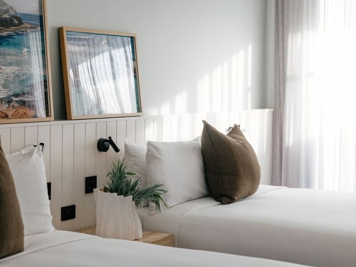 Sunset View Two Bedroom at Elysium Hotels twin beds beside framed coastal art, a plant, and soft grey curtains