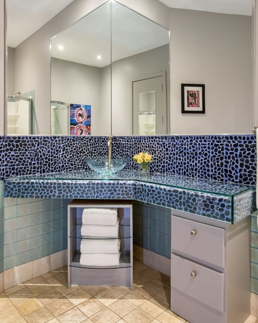 bathroom with glass sink and mirror in front of pebble tile back