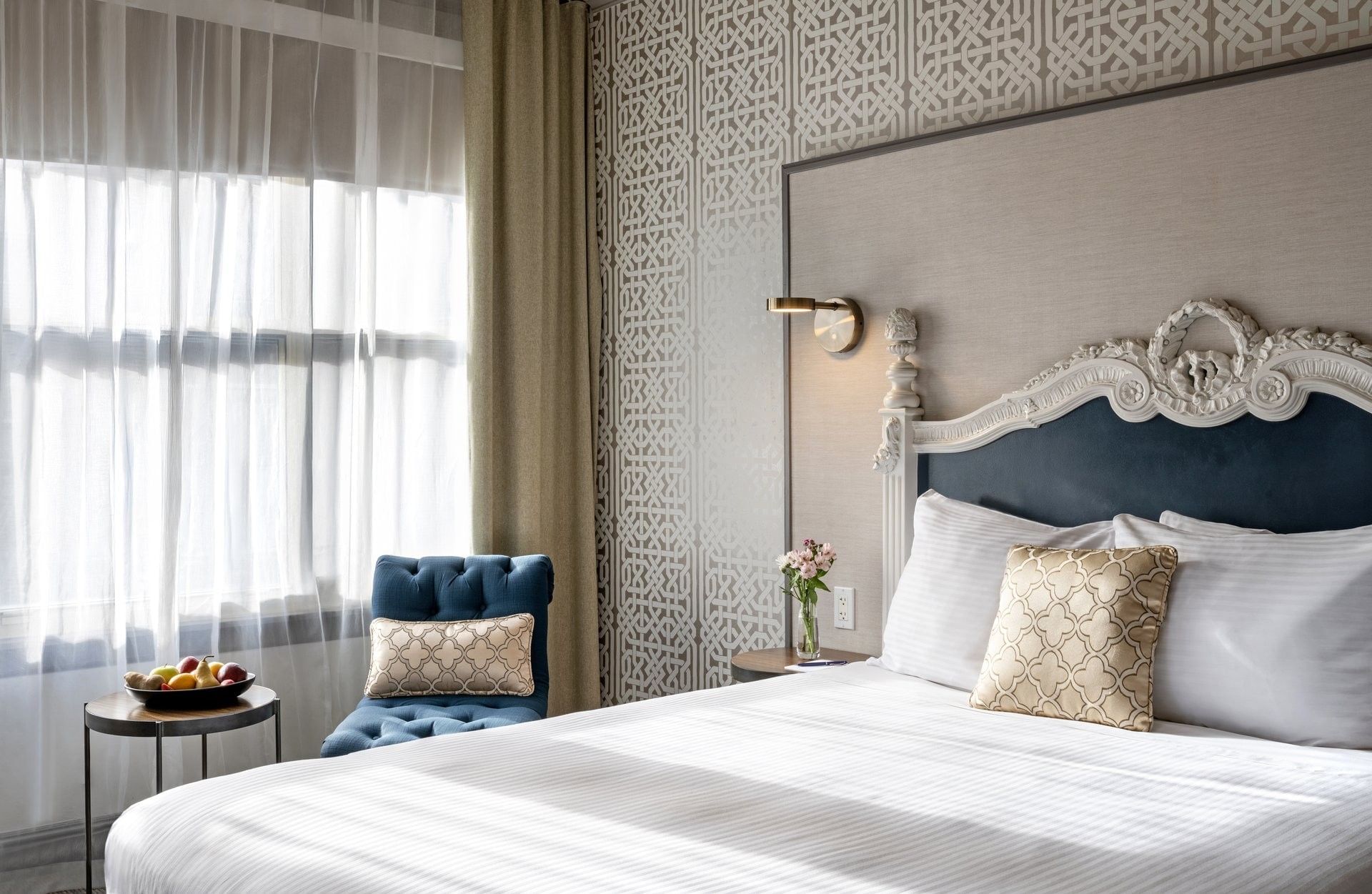 Blue tufted chair by a fruit bowl on a table near a plush bed in Corner Deluxe Room at Warwick San Francisco