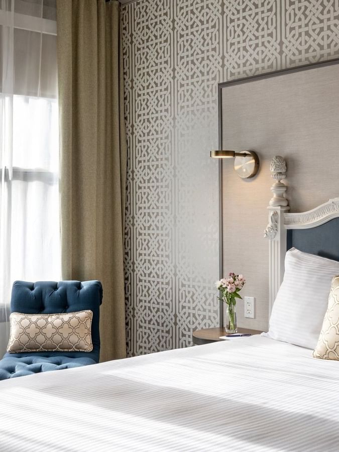 Blue tufted chair by a fruit bowl on a table near a plush bed in Corner Deluxe Room at Warwick San Francisco