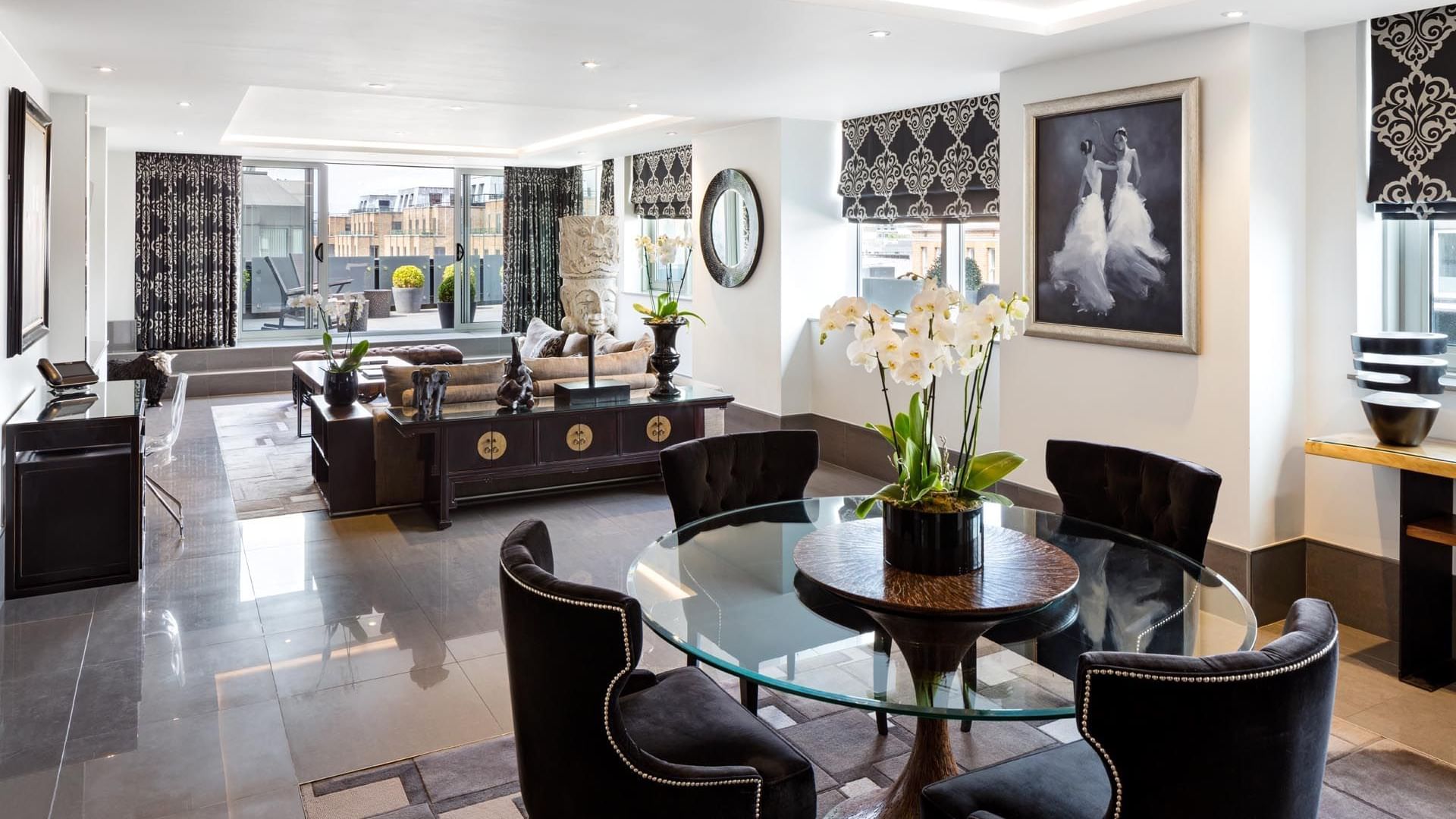 Elegant Ebony Suite living room at The May Fair Hotel featuring a round glass table, black chairs, and white orchids