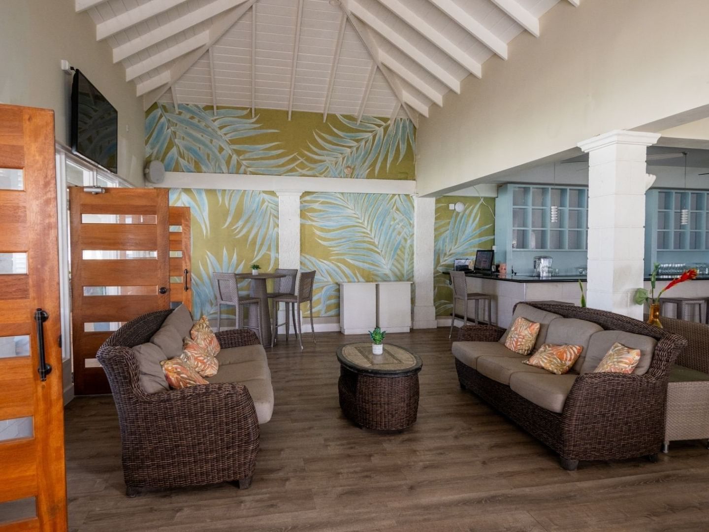 Elegant Savannah Beach Hotel lounge with wicker couches, wooden doors, tropical wall art, and a bar.