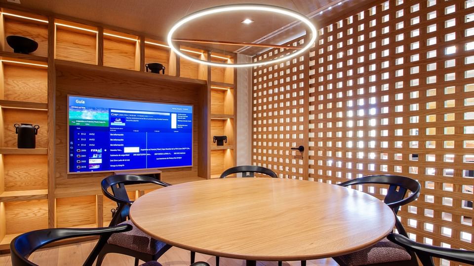 Sala de reuniones de madera con mesa redonda, sillas y TV grande en Camino Real Polanco México
