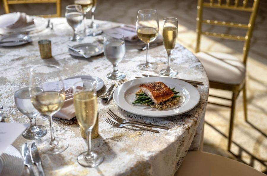 Plate of grilled salmon placed by wine glasses on a tablecloth in Tip Top Tap Ballroom at Warwick Allerton Chicago