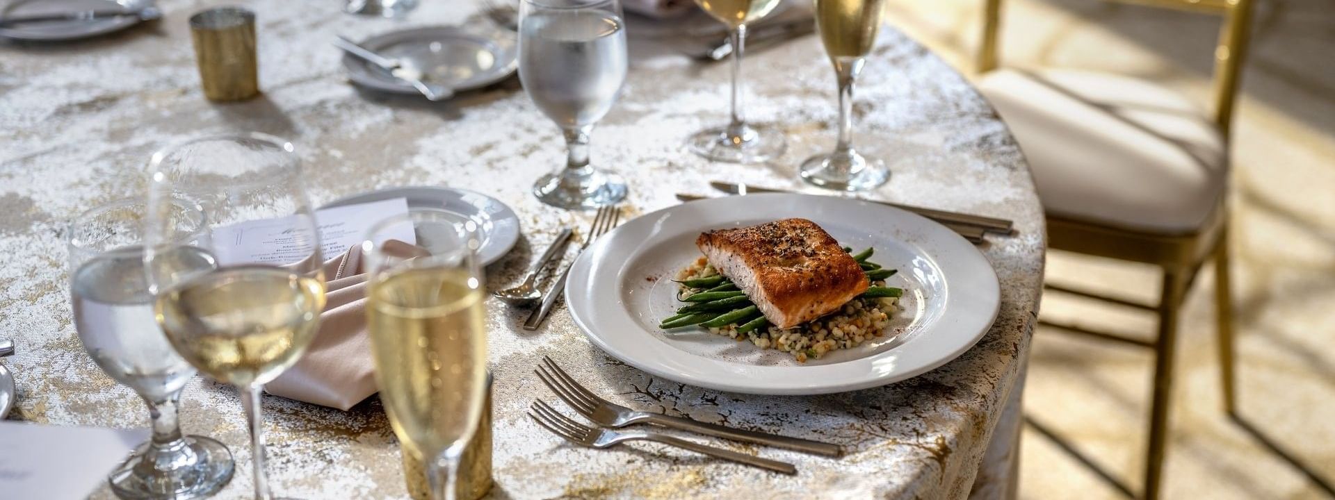 Plate of grilled salmon placed by wine glasses on a tablecloth in Huron Room at Warwick Allerton Chicago