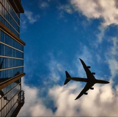 Silhouette of an airplane flying past modern glass skyscraper building under cloudy blue sky near Hotel X Toronto