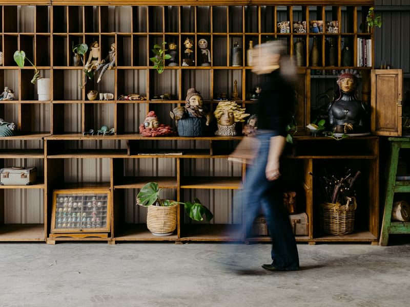 A person walks past wooden shelving displaying artisan ceramics and plants in a creative studio space for Margaret River Open Studios 2026.