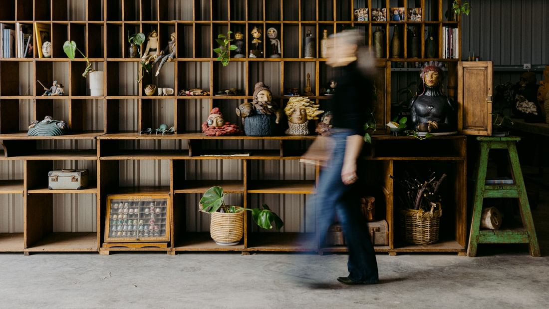 A person walks past wooden shelving displaying artisan ceramics and plants in a creative studio space for Margaret River Open Studios 2026.