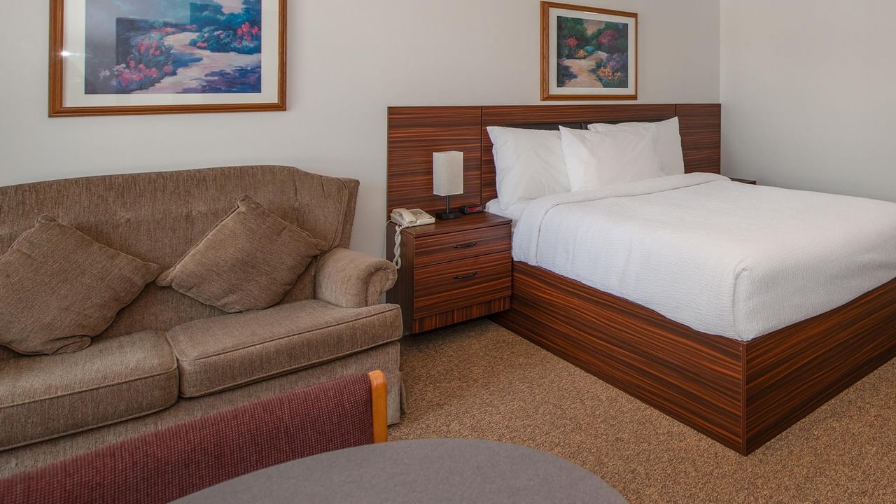 guest room with one bed, sofa, nightstand and wood furnishings at Coast Whitecourt Hotel
