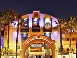 Illuminated City National Grove of Anaheim entrance at night with palm trees and buildings.