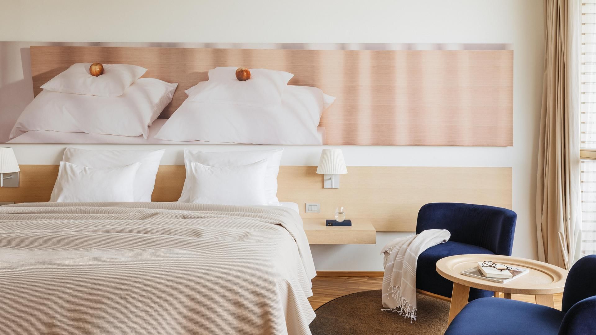 Hotelzimmer mit großem Bett, zwei Sesseln, Couchtisch und Wandbild von zwei Betten.