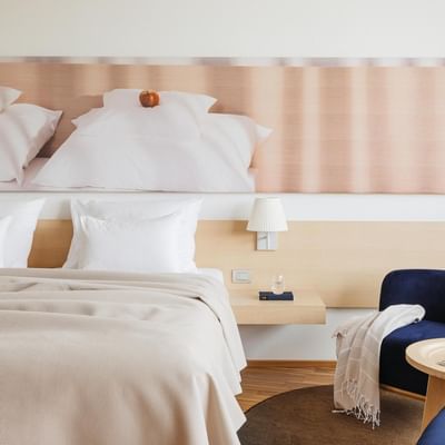 Zimmer mit großem Bett, Nachttischen, zwei Stühlen und rundem Tisch vor einem großen Wandgemälde.
