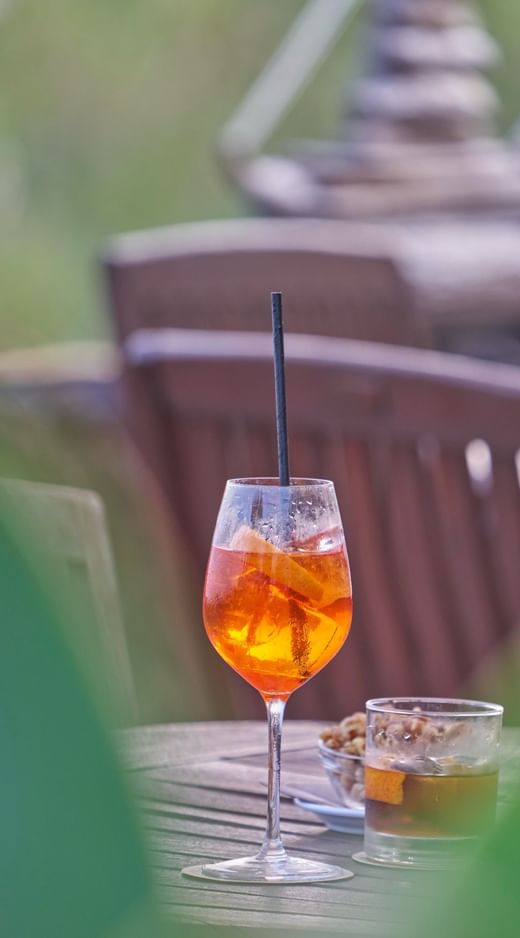 Close-up of an orange cocktail and a drink on a wooden table beside outdoor seating at Caloura Hotel Resort
