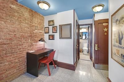 Brick wall room with desk, chair, mirror, toilet, framed pictures, blue ceiling, and a poster on the wall.