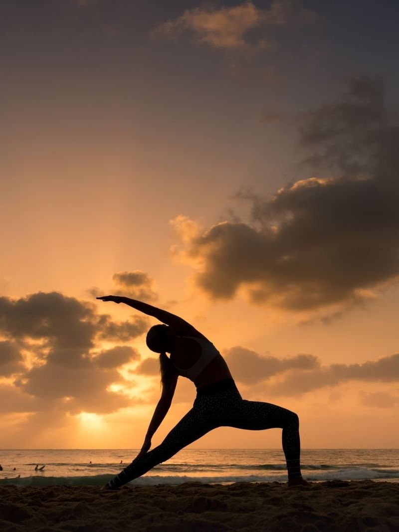 Yoga pose near Elysium Manly featuring a woman in silhouette against ocean waves under a vibrant golden sunset sky
