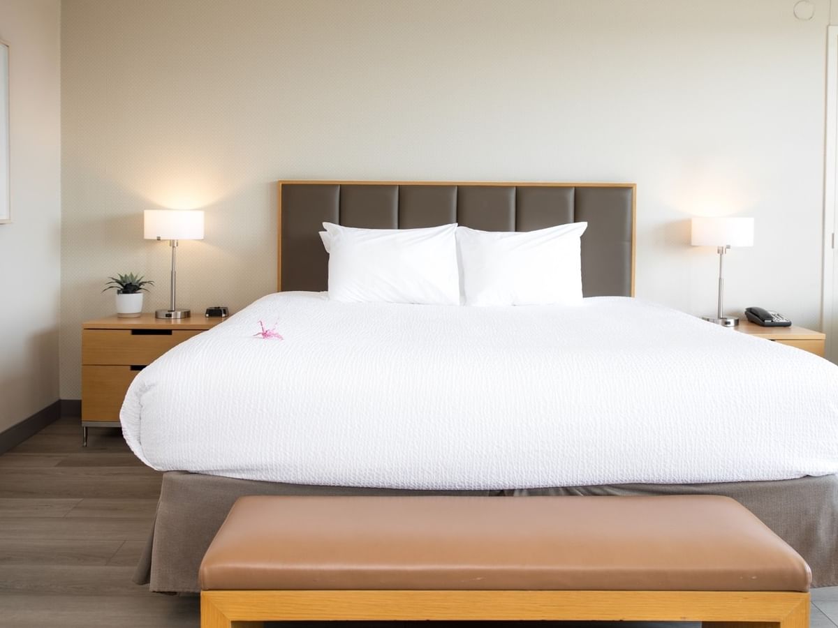 Clean hotel bedroom with large bed, two nightstands, lamps, artwork, and a chair.