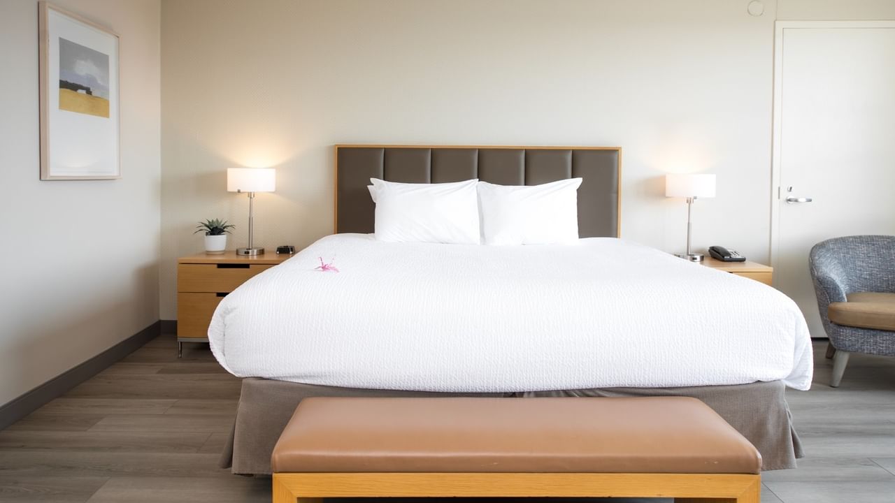 Clean hotel bedroom with large bed, two nightstands, lamps, artwork, and a chair.