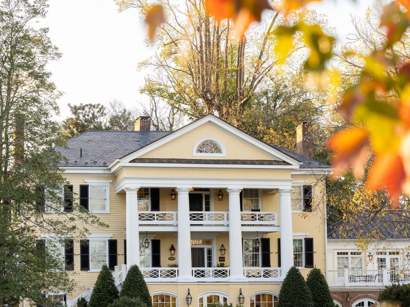 Elegant yellow house with white columns and autumn leaves in the Inn at Willow Grove