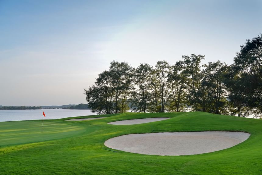 Lakeside golf green with a flag and white sand bunkers beneath green trees at Clemson University Conference Center & Inn