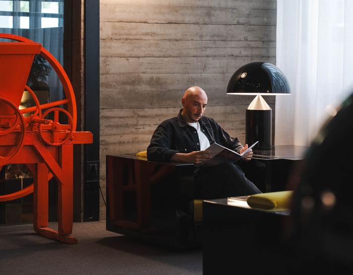 Uomo con libro seduto su poltrona con lampada, luce e macchinario rosso a DUPARC Contemporary Suites