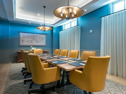 Boardroom with blue walls, yellow chairs around wooden table, and brass chandeliers at Camp Creek Inn in Inlet Beach.