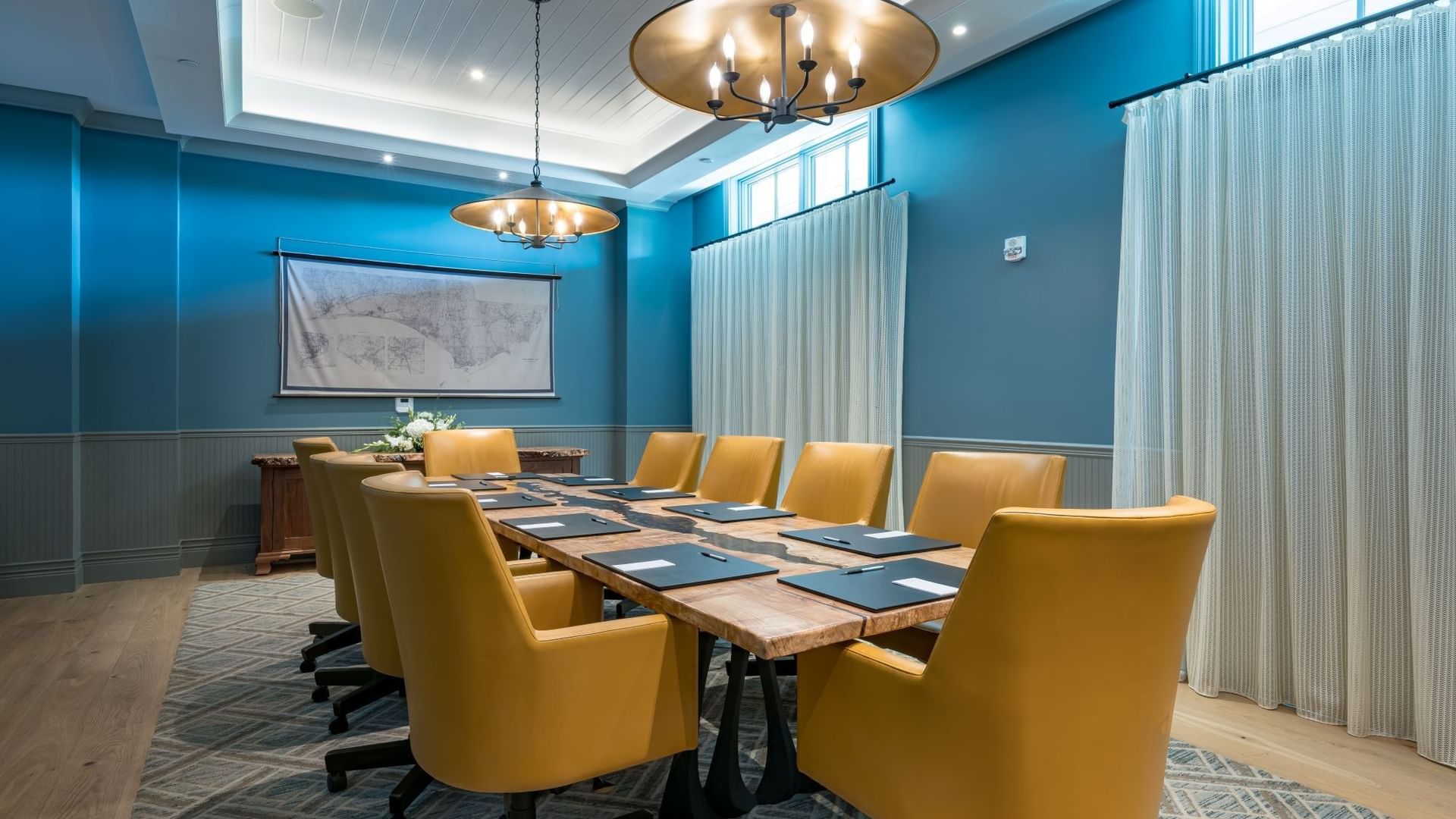 Boardroom with blue walls, yellow chairs around wooden table, and brass chandeliers at Camp Creek Inn in Inlet Beach.